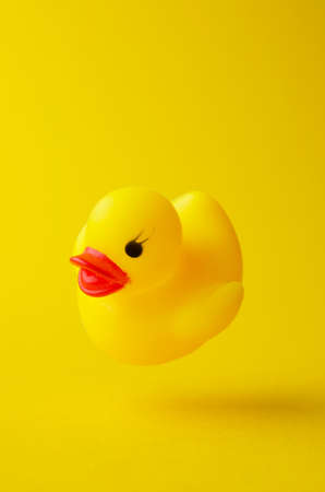 Yellow rubber duck floating in the air over bright yellow background