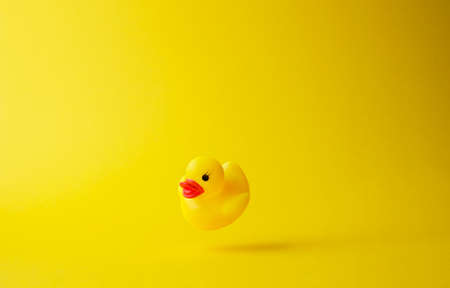 Yellow rubber duck floating in the air over bright yellow background