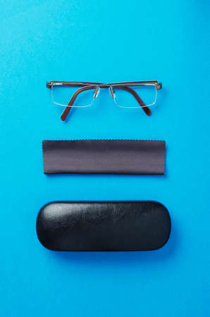 Eye glasses, case and fabric organized over blue background, above view.の写真素材