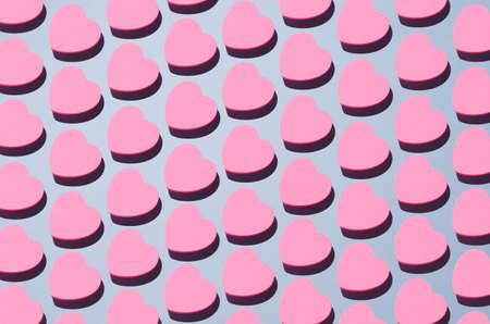 Pink heart shaped sticky notes organized in a row over blue background, top view with negative space
