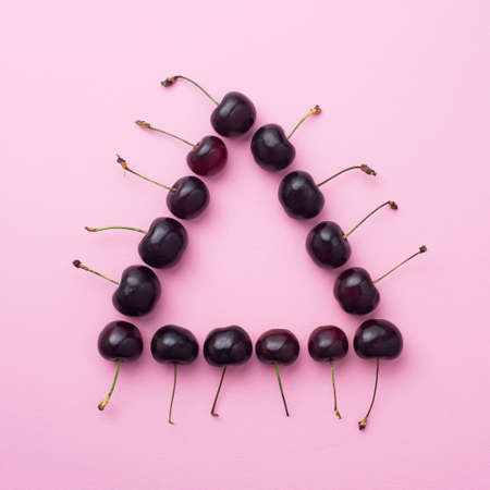 Multiple cherries organized in a triangle shape over pink backgroundの写真素材