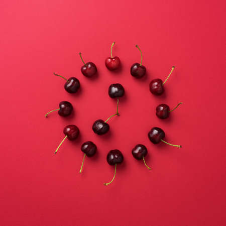 Multiple cherries organized in a shape of a clock over red backgroundの写真素材