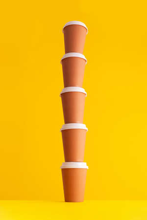 Multiple disposable coffee cups organized in a stack over yellow backgroundの写真素材