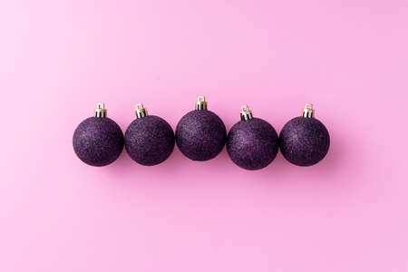 Purple Christmas baubles organized in a row over pink background, top view