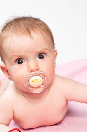 Seven months old infant staring confused at the camera with a pacifier in his mouth