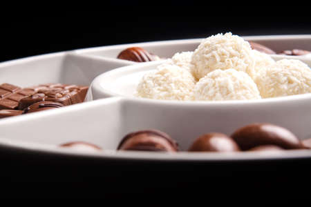 White coconut  and brown chocolate balls on plate, isolated on black background 