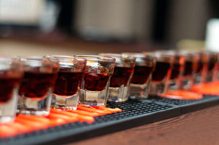 Red, strong alcoholic drink in small glasses on bar waiting to be servedの写真素材