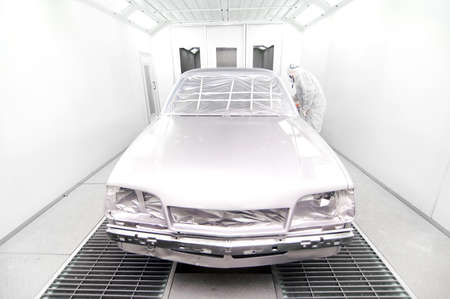 Worker using a paint spray gun for painting a car in special boxの写真素材