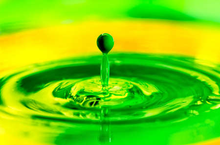Green liquid paint drop splashing in yellow color 