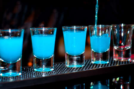 Bartender pours blue alcoholic drink into small glasses on bar with black backgroundの写真素材