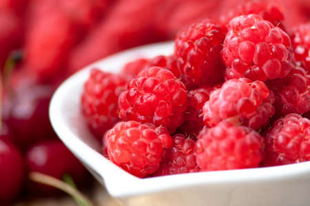 Organic and healthy raspberry in white bowl with wild berries on background