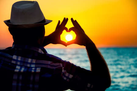 silhouette of a Man showing love  with fingers in the sunset on beachの写真素材
