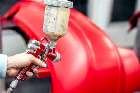 Close-up of spray gun with red paint painting a car in special boothの写真素材