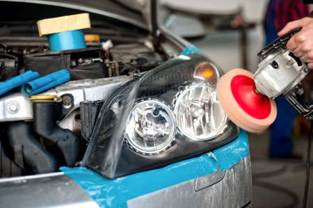 auto mechanic working on polishing a car headlight with power buffer machine in car care system