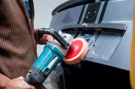professional mechanic cleaning the metal surface of the bodywork of a car with power buffer machine....