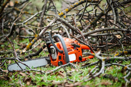 Gasoline professional chainsaw cutting branches against wood background 