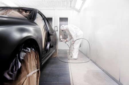 worker painting a black car in a special garage, wearing a white costumeの写真素材