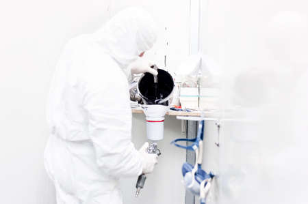 Auto worker preparing black paint for body work on a car wearing white special suit