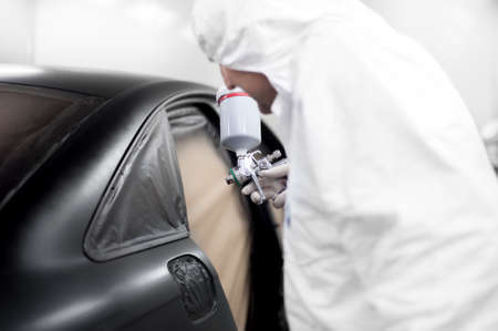 auto worker spraying black paint on a car in an auto garageの写真素材