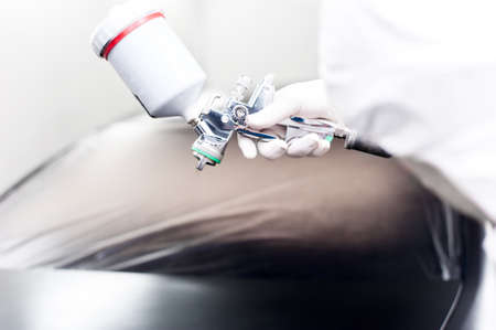 Close-up of spray gun with black paint painting a car in special boothの写真素材