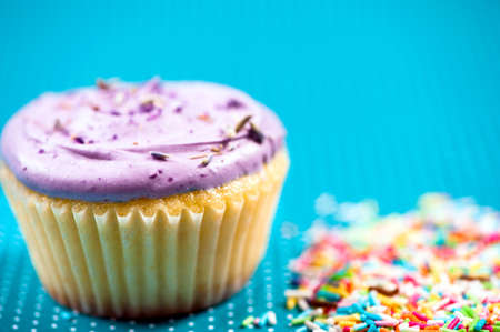 close-up of a colorful muffin with vanilla and fruits topping and candy against blue background