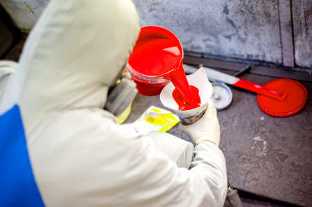 Auto mechanic mixing and pouring red paint for spraying and painting cars in industrial factory