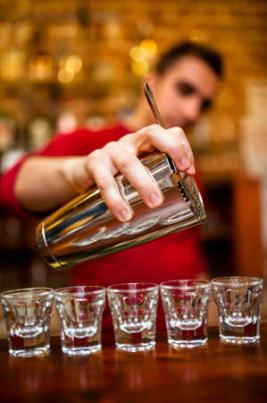 Close-up of Barman pouring alcoholic drink and cocktails into small glasses on bar counter