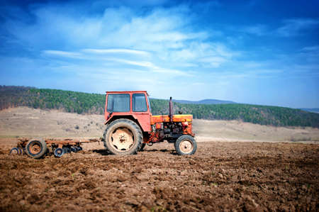 agriculture and harvesting - Vintage tractor plowing and cultivating the field under the blue sky
