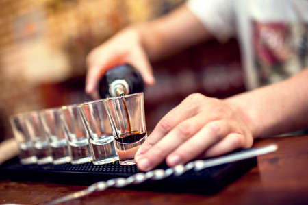 Bartender pouring brown alcoholic cocktail in glasses on barの写真素材