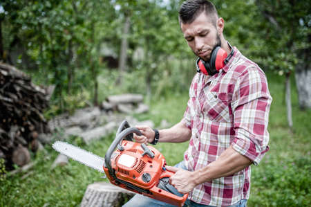 portrait of sexy and hansome man with chainsaw and protective gear ready for cutting woodの写真素材