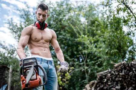 portrait of sexy man with chainsaw and protective gear ready for cutting wood の写真素材