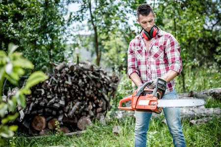portrait of aggressive, muscular and athletic man with chainsaw getting ready for fire wood cutting