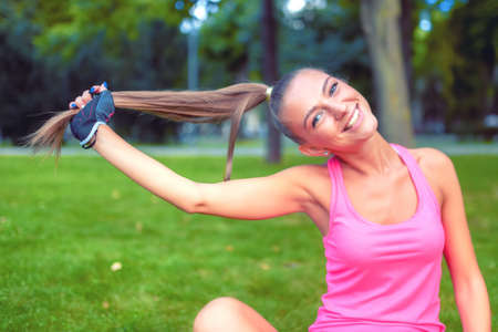 smiling blonde girl playing with hair while working out in parkの写真素材