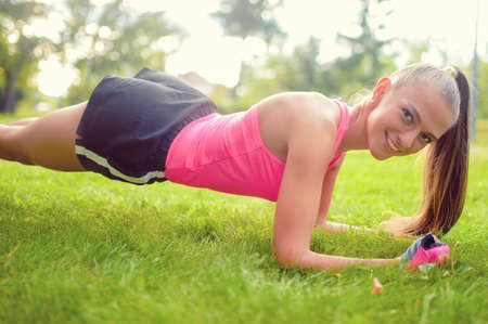 blonde athletic girl stretching and making exercises on grass in parkの写真素材