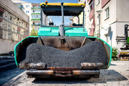 industrial paver laying fresh asphalt and bitumen pavement on top of gravel layer during road...