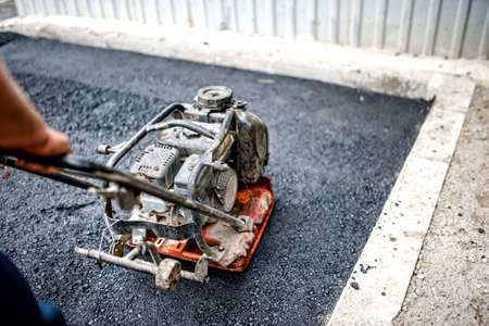close-up of asphalt worker in construction site with manual compactor plate