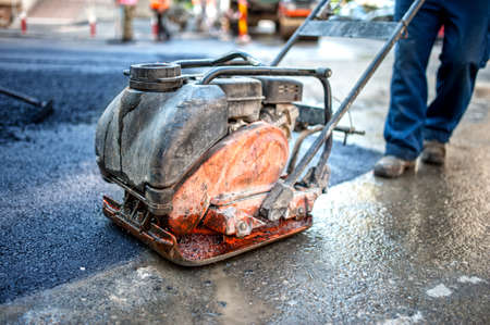 asphalt worker at road construction site with compactor plate and toolsの写真素材