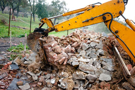 excavator on demolition site loading bricks and concrete walls