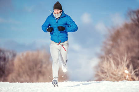 Fitness concept of a man running outdoor in snow on a cold winter dayの写真素材