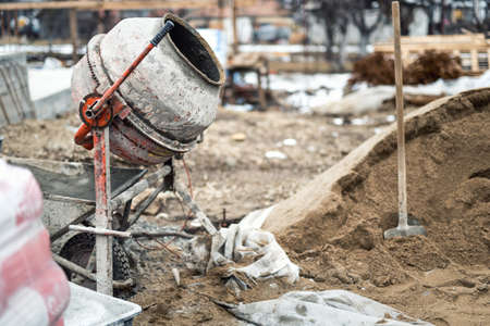 Industrial cement mixer machine at house construction site. Concrete mixer, sand and tools at building siteの写真素材