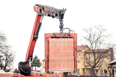 Crane delivers a brick pallet at building construction site, isolated on white skyの写真素材