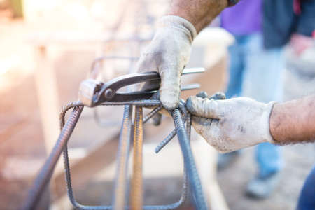 worker using pincers and steel wire to secure bars for concrete pouringの写真素材