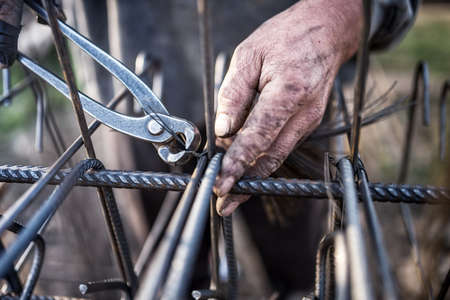 Details of construction worker - hands securing steel bars with wire rod for reinforcement of concrete or cementの写真素材