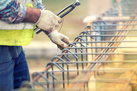 worker hands using steel wire and pliers to secure bars on construction site and preparing for concrete pouringの写真素材
