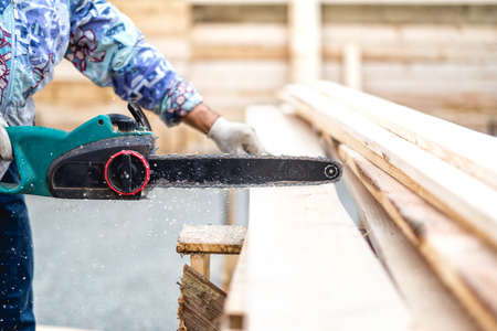 worker, lumberjack or handyman cutting timber planks with electric chainsawの写真素材
