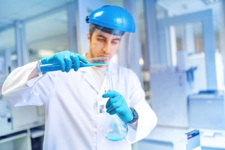 young male scientist learning and making experiments in chemical laboratory with liquid substances