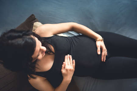 Portrait of future mother laying on bed, maternity shooting concept. Happy pregnant woman holding bellyの写真素材