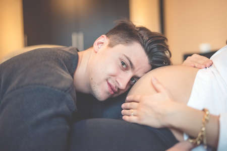 portrait of the future father, hugging, kissing and  listening pregnant wife belly. Soft effectの写真素材
