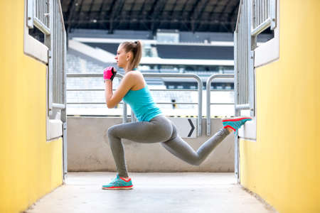 Female runner stretching and doing squats after jogging training. Fitness concept on stadium
