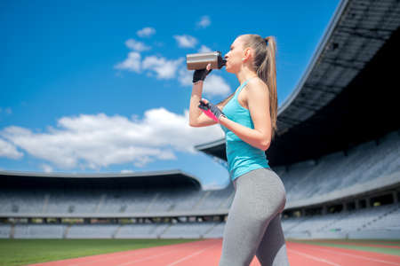 Portrait of healthy fitness girl drinking protein shake during workout on stadiumの写真素材